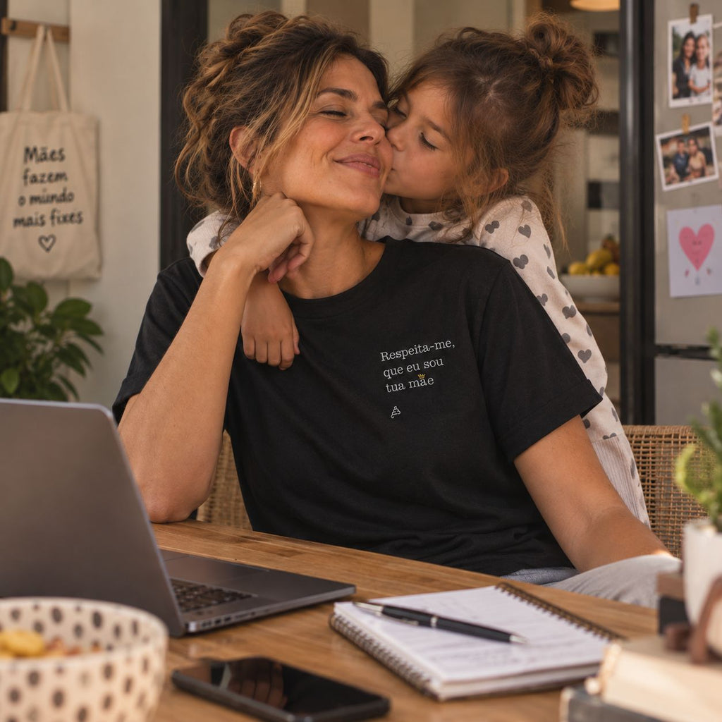 Mãe com T-shirt preta bordada com a frase “Respeita-me, que eu sou tua mãe” da Poesia Cocó, acompanhada pela filha