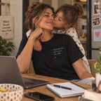 Mãe com T-shirt preta bordada com a frase “Respeita-me, que eu sou tua mãe” da Poesia Cocó, acompanhada pela filha