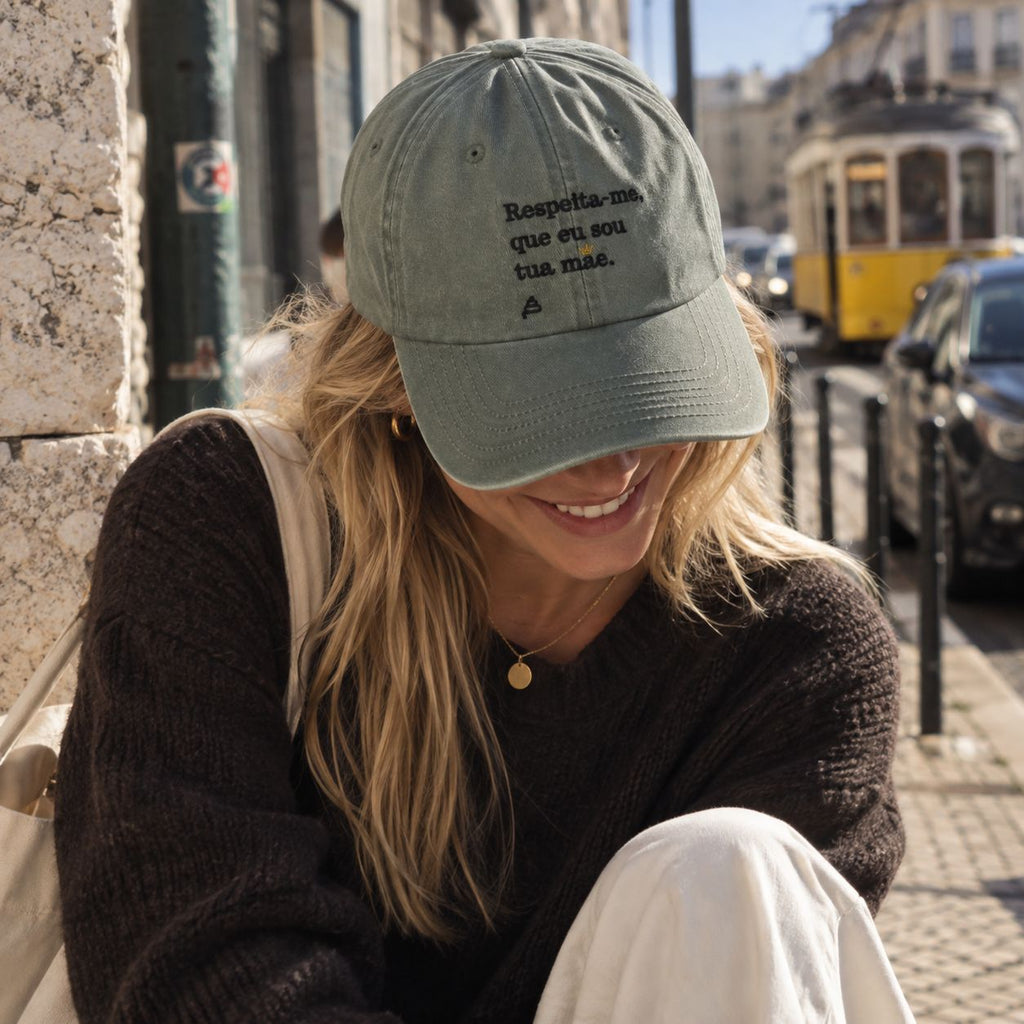 Mulher com boné verde bordado “Respeita-me, que eu sou tua mãe.” da Poesia Cocó