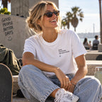 Mulher com T-shirt branca bordada com a frase “Quem tem friends não morre na jail” da Poesia Cocó