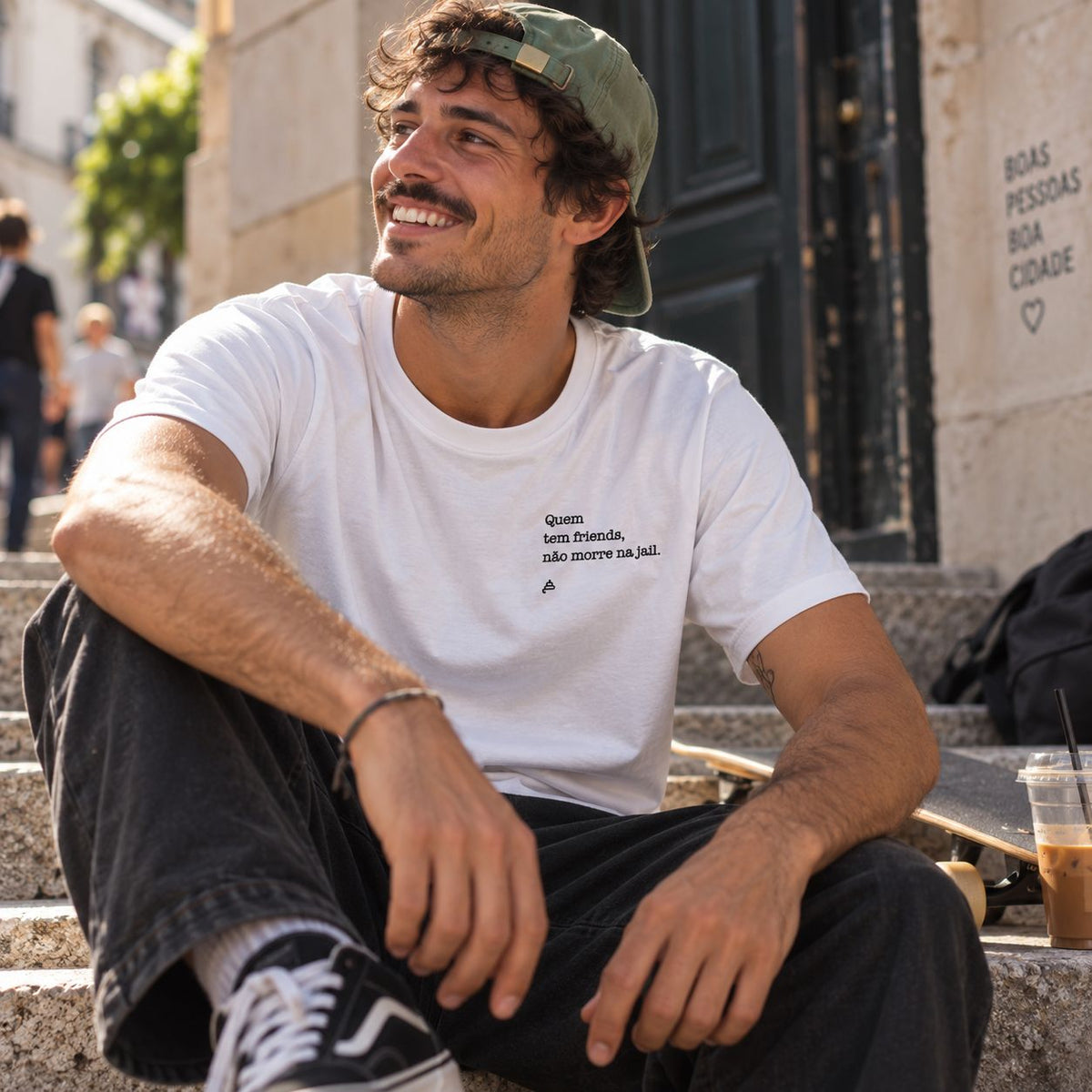 Homem com T-shirt branca bordada com a frase “Quem tem friends não morre na jail” da Poesia Cocó
